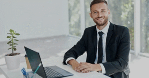 Homem de terno sentando em frente a uma mesa com um notebook.